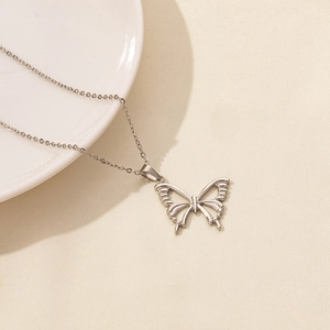 Close-up of a silver butterfly pendant on a delicate chain over a white plate