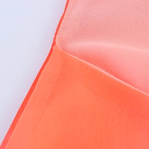 Macro shot showing the fine weave texture and stitching of the orange chiffon dress fabric