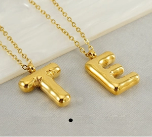 Detail of polished gold stainless steel T and E bubble initial pendant necklaces