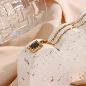 Macro detail of square black gemstone pendant with white crystal frame on gold water wave chain