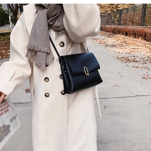 Détail d'un sac bandoulière en cuir noir avec fermoir en métal doré dans un parc d'automne