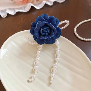 Detailed view of navy denim rose hair clip with pearl tassels on a white ceramic plate
