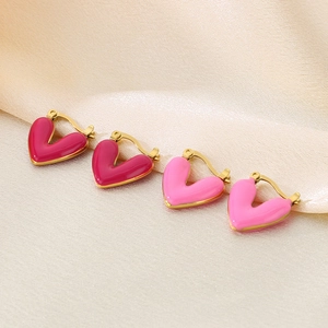 Detail of pink heart-shaped enamel earrings with gold plating on beige silk