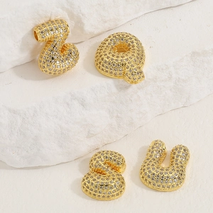 Detail of golden bubble letters Z, Q, S, U with white cubic zirconia on white stone