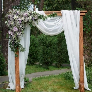 Wedding wooden arch decorated with white chiffon drapes and purple floral arrangements