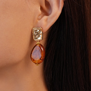 Close-up of model wearing amber resin teardrop earrings with textured gold metal square studs