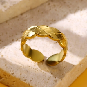 Close-up of golden geometric cross ring with rhombus pattern on beige stone texture