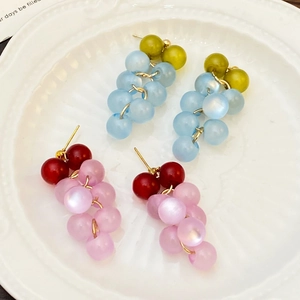 Detailed macro view of grape-shaped beaded earrings in colorful translucent resin on white tray