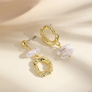 Macro detail of asymmetric gold hammer-textured hoop earrings with white baroque pearls