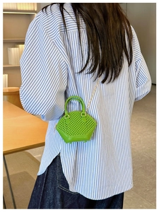 Green mini shell handbag with woven texture and gold chain shown in a cafe setting
