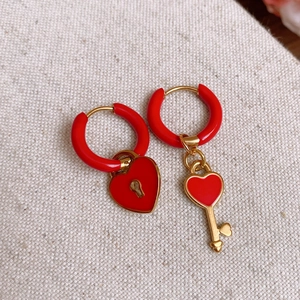 Macro shot of asymmetrical gold earrings with red enamel heart lock and key charms
