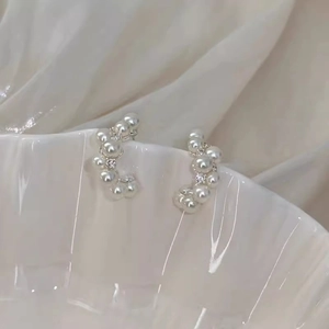 Macro detail of elegant C-shaped pearl and diamond earrings on white ceramic