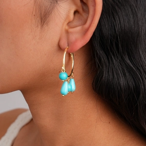 Close-up of bohemian gold hoop earrings with turquoise teardrop beads on a model