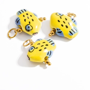 Macro shot of three yellow ceramic fish pendants with blue fins and gold metal hooks
