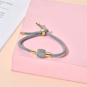 Détail macro du bracelet en cordon tressé gris avec pierre carrée sur support géométrique