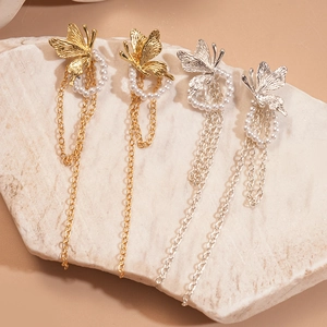 Elegante goldene und silberne Schmetterlingsperlen-Ohrringe auf neutralem Steinuntergrund
