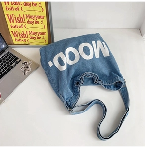 Flat lay of denim tote bag with white MOOD text and shoulder strap on minimalist desk