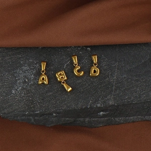 Macro shot of 18K gold plated bubble initial pendants A, B, C, D on a dark stone base