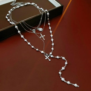 Detail view of silver layered chain necklace with white pearls and cross medal pendants