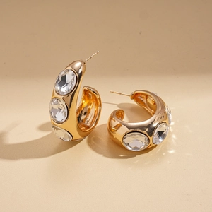 Close-up of gold-plated chunky C-shaped earrings with large inlaid sparkling crystals