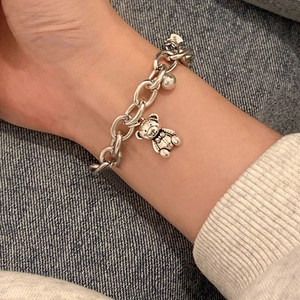 Minimalist silver metal chain bracelet with a teddy bear charm worn on a female wrist