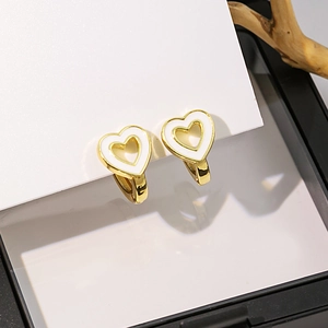 Détail de boucles d'oreilles cœur doré avec émail blanc sur support minimaliste