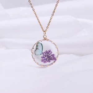 Close-up of glass pendant with blue butterfly and purple dried flowers on gold chain