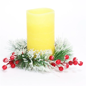 Close-up of yellow pillar candle with pine needles, red berries and snow base wreath