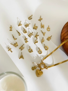 Detailed flat lay of 26 gold alphabet heart charms with pearls and a gold snake chain necklace