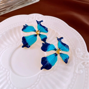 Détail macro de boucles d'oreilles fleur émail bleu dégradé avec cœur doré sur plat