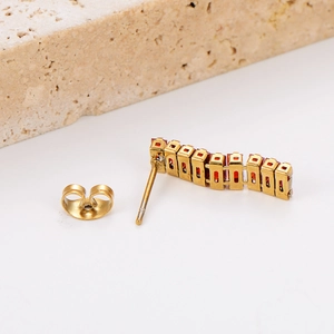 Macro shot of gold curved stud earrings with red rectangular zircon stones on white background