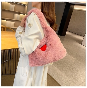 Close-up of pink plush shoulder bag with a red heart decoration on a female model