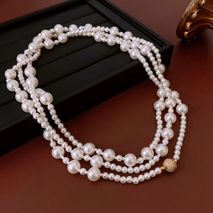 Détail d'un collier de perles multicouche avec un fermoir sphérique doré serti de zircons