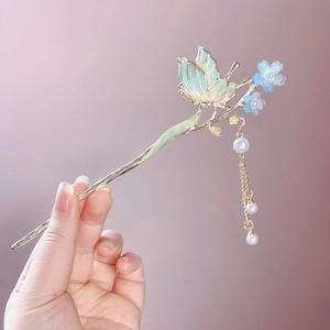 Gros plan d'une épingle à cheveux papillon dorée avec fleurs bleues et pampilles