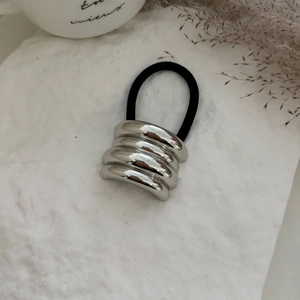 Detail of silver alloy bow hair tie with textured metallic finish on white stone surface