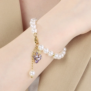 Close-up of pearl bead bracelet featuring a sparkling purple grape pendant on a model wrist