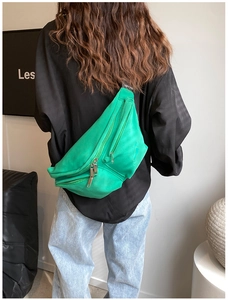 Back view of a vibrant green nylon crossbody bag with wide strap on a model outfit