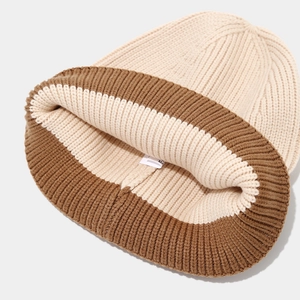 Close-up of thick beige and brown knit beanie with textured ribbed cuff and white label