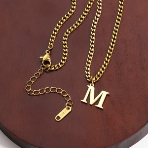 Detailed macro view of 18K gold plated stainless steel letter M pendant on a cuban chain