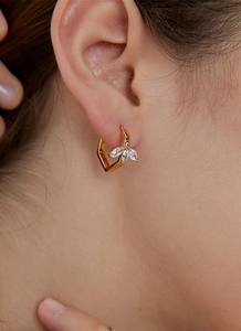 Detailed close-up of leaf-shaped gold-plated zircon earrings worn on a model's ear