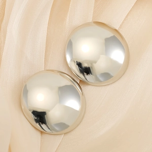Close-up of polished silver round geometric earrings on soft beige fabric texture