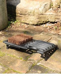 Detail of vintage cast iron boot scraper with natural coir bristles on stone path