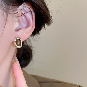 Close-up of vintage gold oval stud earring with brown tiger eye stone on model ear