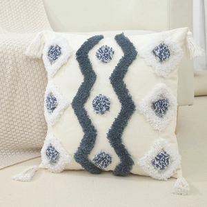 Fodera per cuscino boho crema con nappe blu e frange su un accogliente divano beige