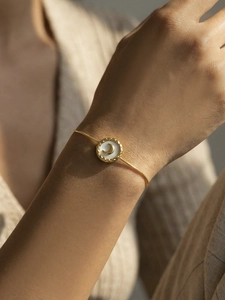 Close-up of a gold snake chain bracelet with a white shell moon pendant on woman wrist