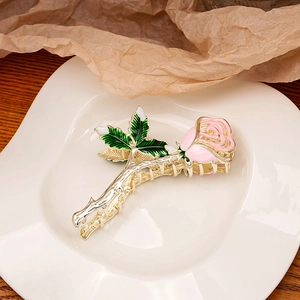 Detailed view of metal rose hair claw with pink petals and green leaves on a white plate
