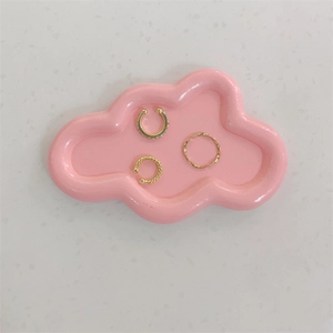 Detailaufnahme von Goldring und Ohrmanschetten auf rosa wolkenförmiger Schmuckschale