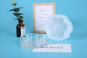 Macro detail of cat paw silicone mold and clear resin dish on a light blue background