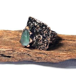 Détail d'une bague en bronze faite main avec pierre verte brute sur fond d'écorce
