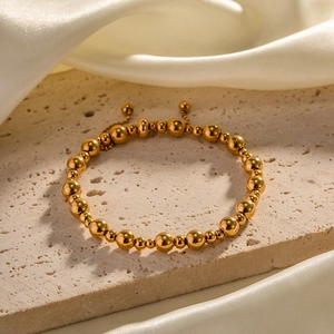 Nahaufnahme von 18K vergoldetem Edelstahl-Perlenarmband auf beigem Stein und Seidenstoff